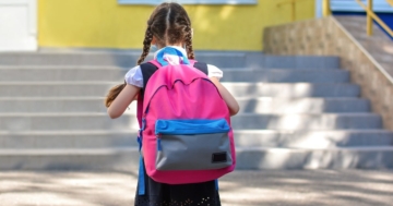 bambina di schiena con zaino sulle spalle che sta per cominciare la prima elementare a settembre