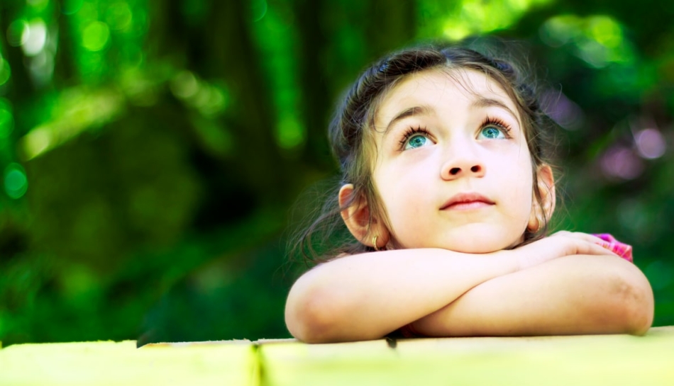 Primo piano di bambina che guarda pensierosa verso l'alto, appoggiata sugli avambracci