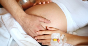 mani di mamma e papà sul pancione in sala parto