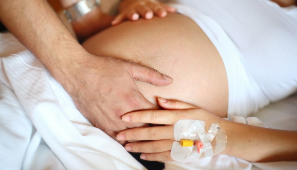 mani di mamma e papà sul pancione in sala parto